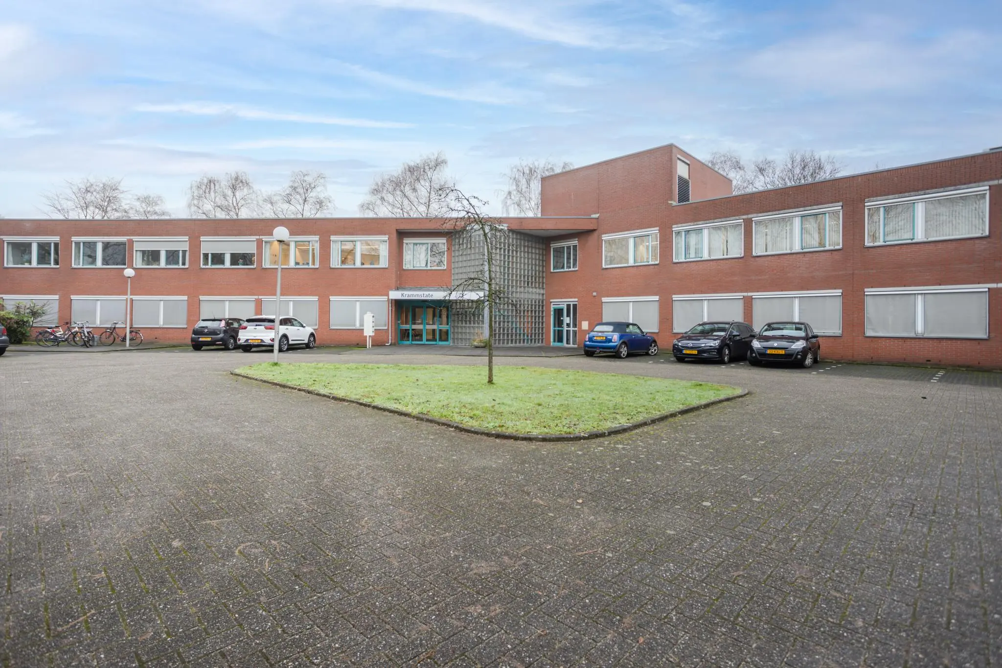 Vooraanzicht van het rode bakstenen gebouw aan de Christiaan Krammlaan met parkeervakken en fietsenrekken.
